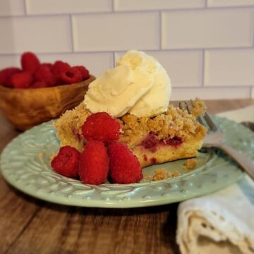 finished plated raspberry buckle with ice cream on top, garnished with fresh raspberries, bowl of raspberries shown in background