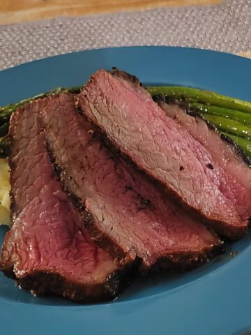 Plated Tri tip steak, sliced with grilled asparagus and mashed potatoes