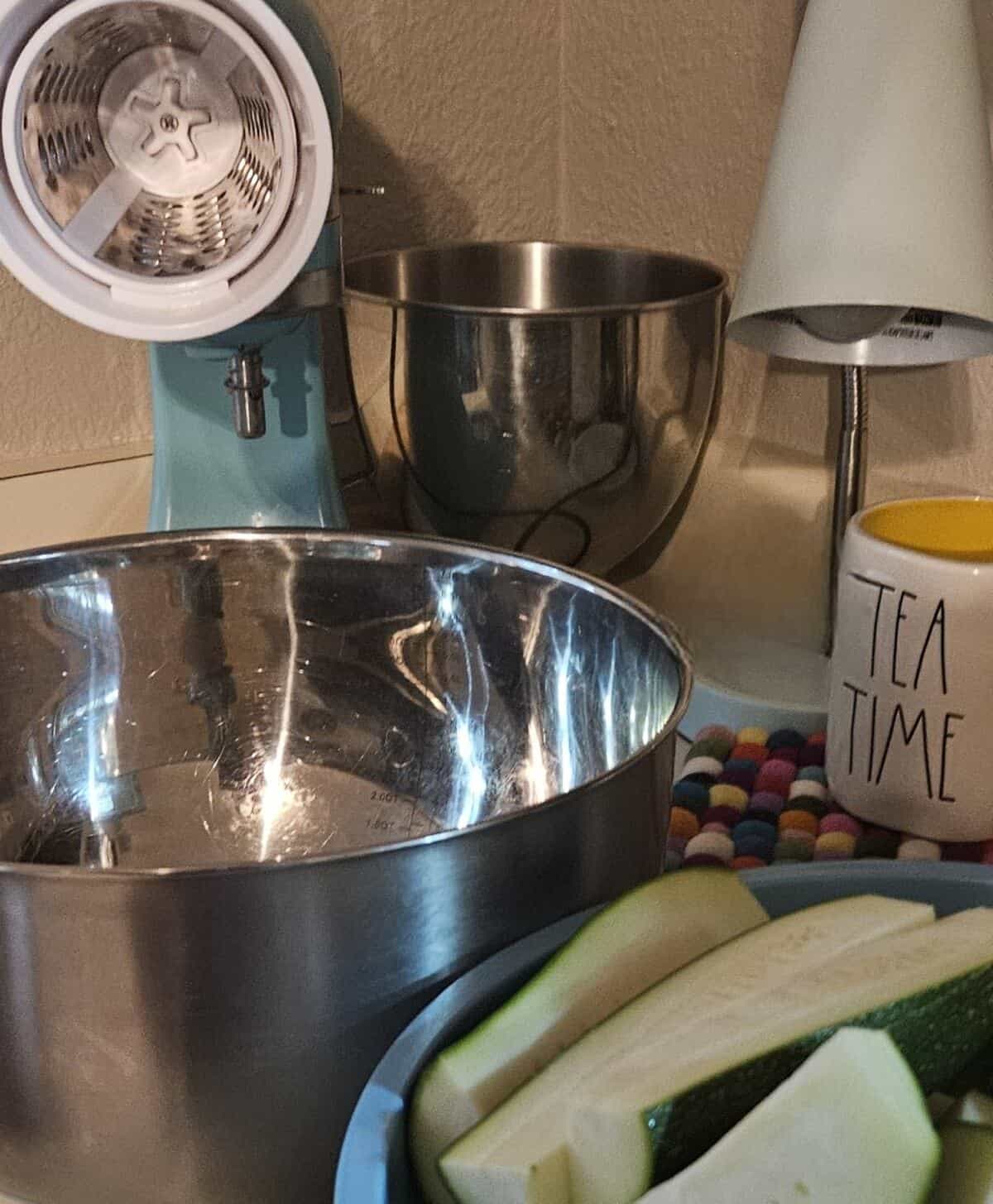 a kitchenaid mixer shown with the shredder wheel attachment, zucchini cut into wedges, ready to be shredded