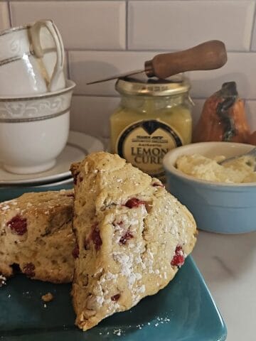 plated red currant scones with a ramekin of clotted cream, a jar of lemon curd, and tea cups