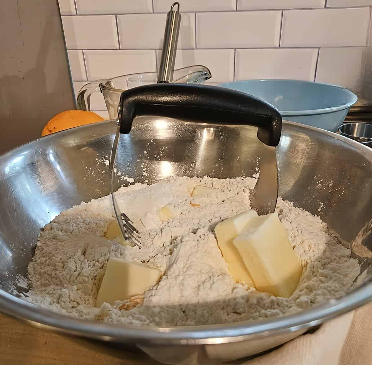 butter chunks and flour in mixing bowl with pastry cutter sticking out of it.