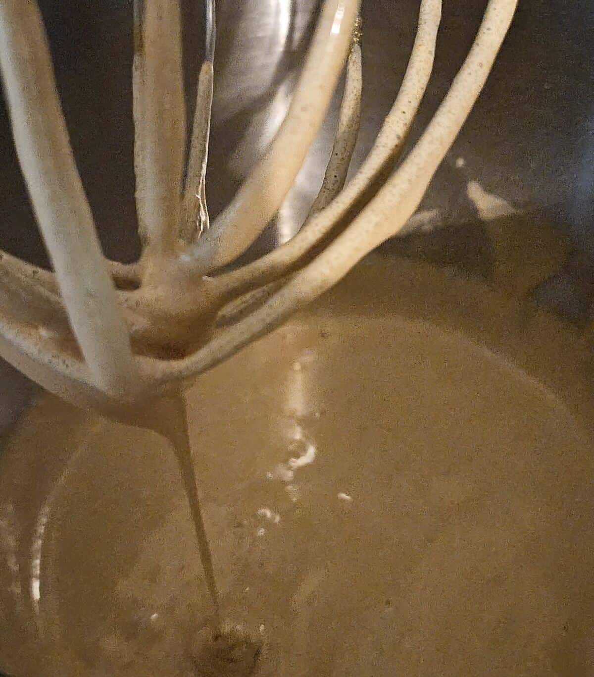 liquid batter dripping from the whip attachment of a stand mixer into a steel bowl