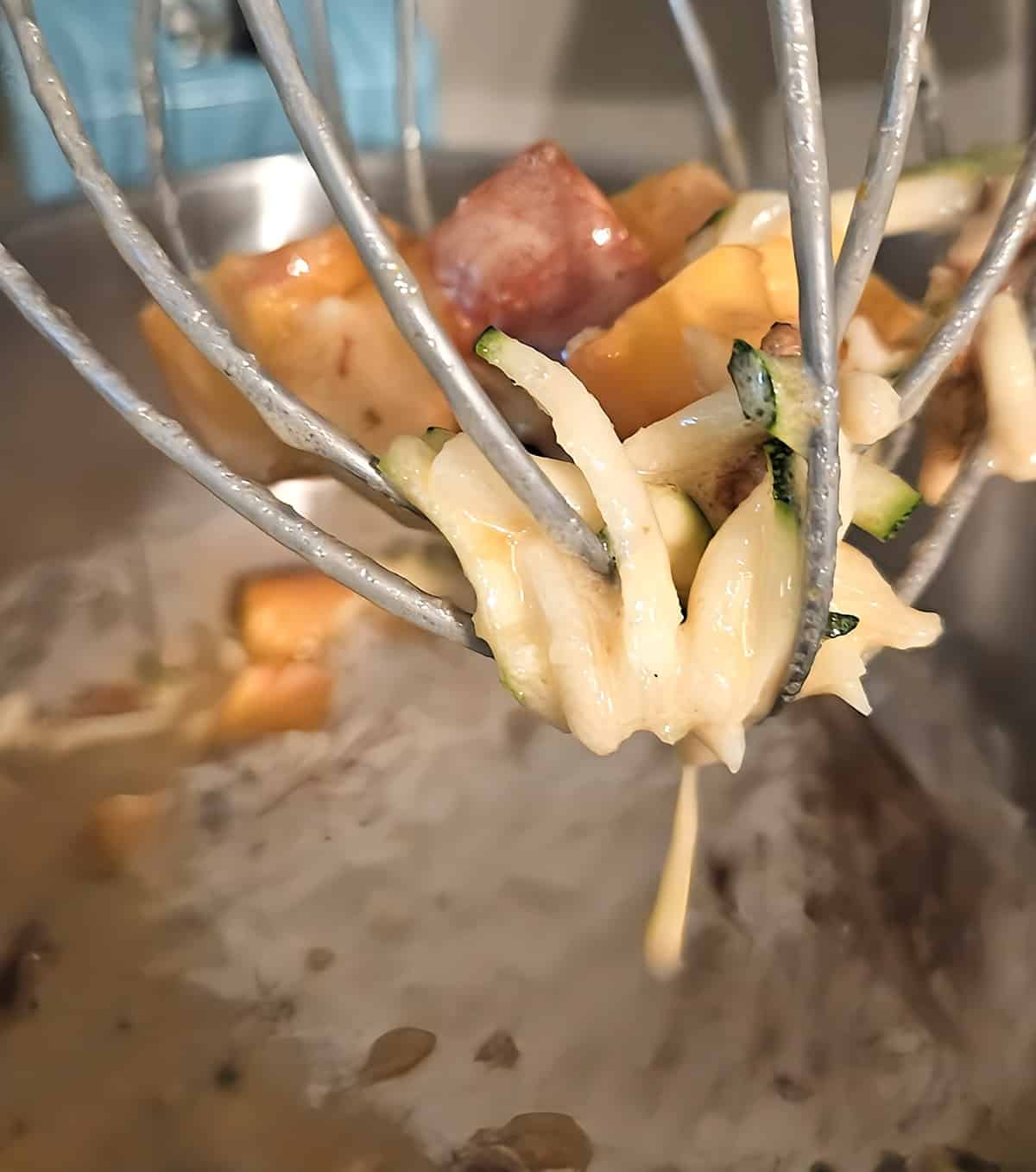 mixer attachment with batter coated peaches and zucchini lodged in it, batter in bowl in background