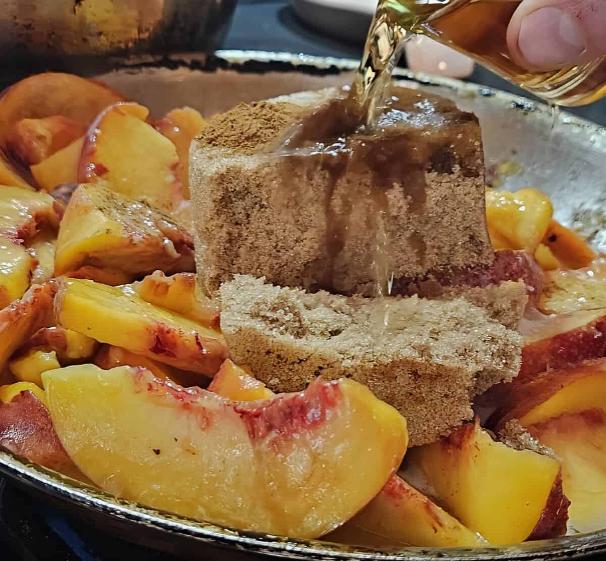 peaches, brown sugar, and cinnamon in pan, bourbon being poured in.