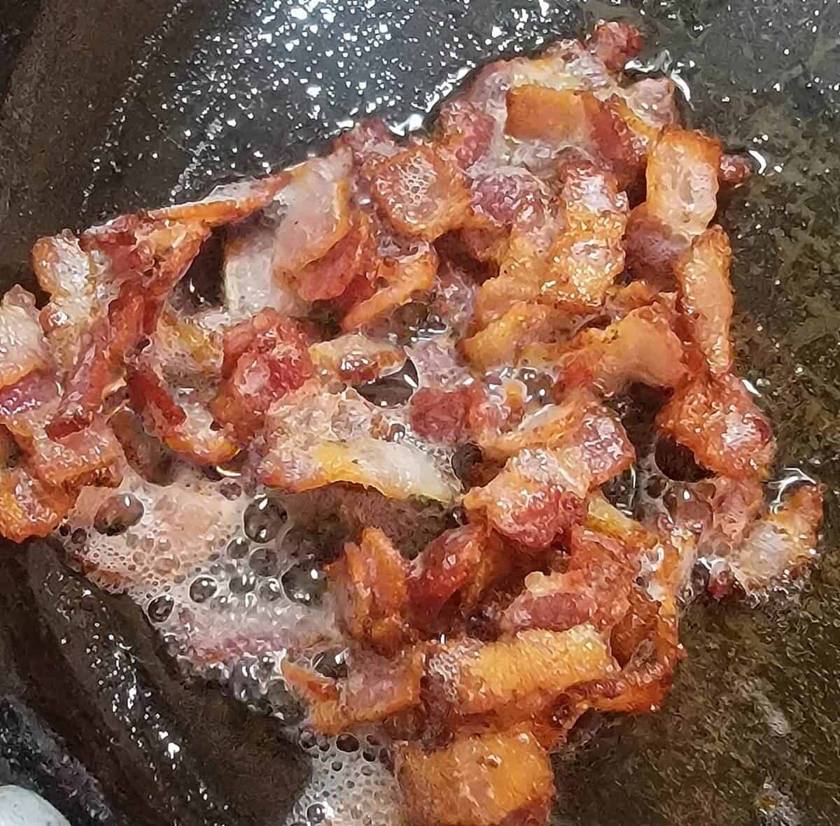 bacon pieces sizzling and browning in skillet