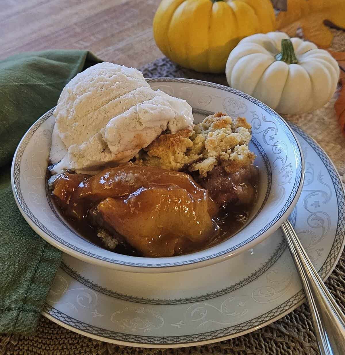 finished portion of peach cobbler in bowl with a scoop of vanilla ice cream, a spoon, and cloth napkin