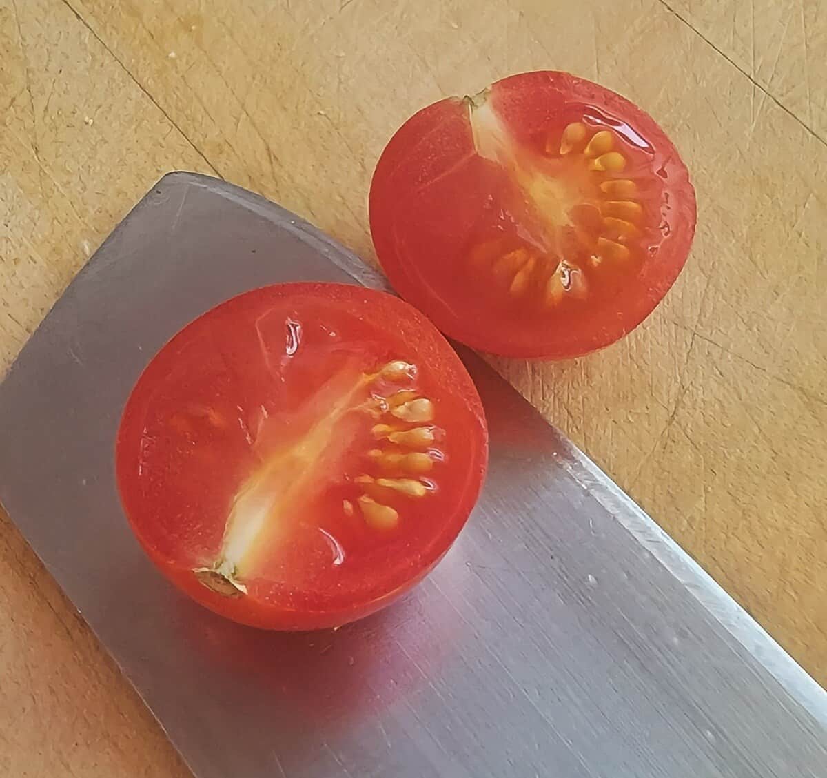 a single cherry tomato cut in half on a cutting board with a knife