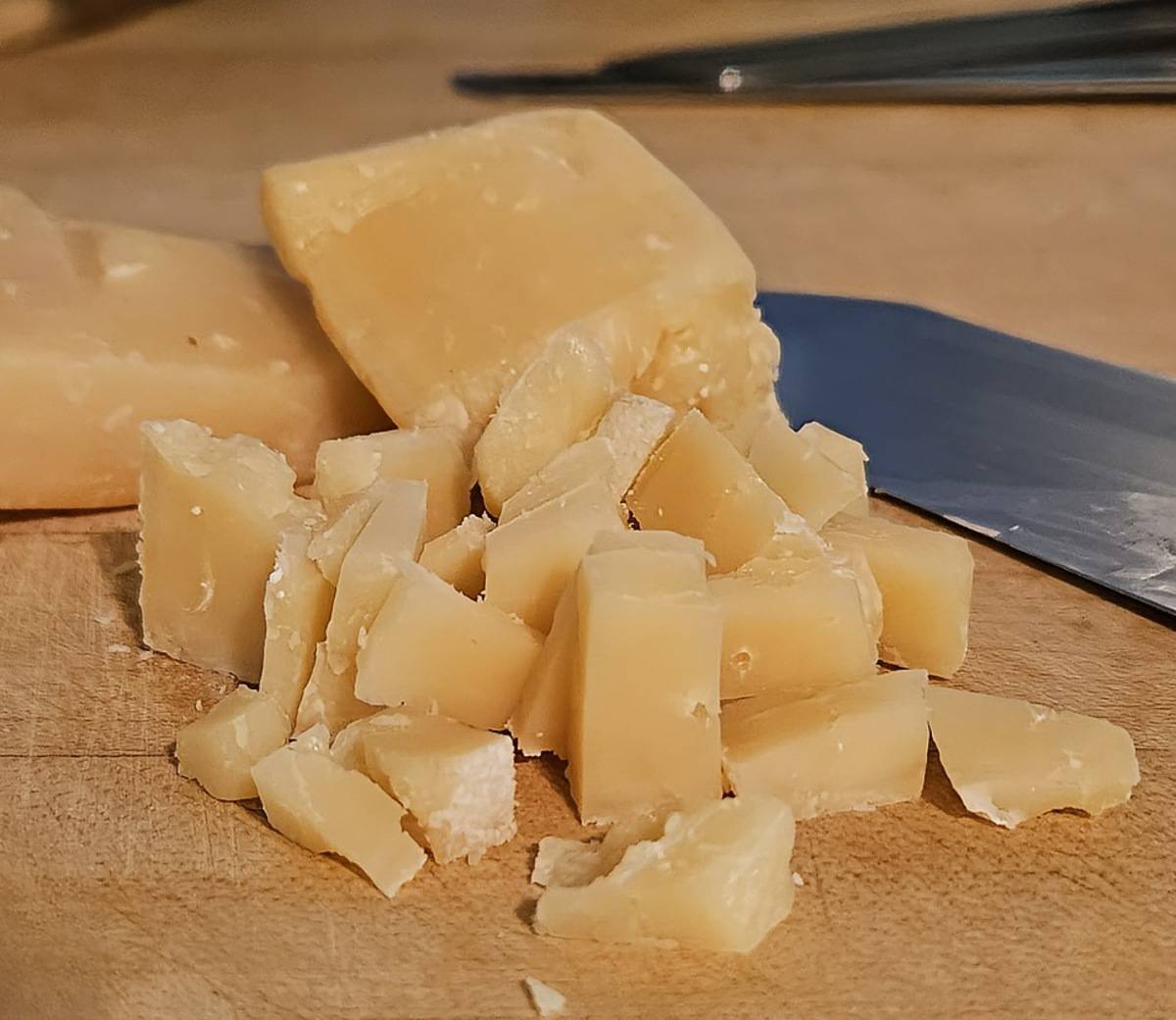 roughly chopped parmigiana Reggiano on a wooden cutting board with a knife