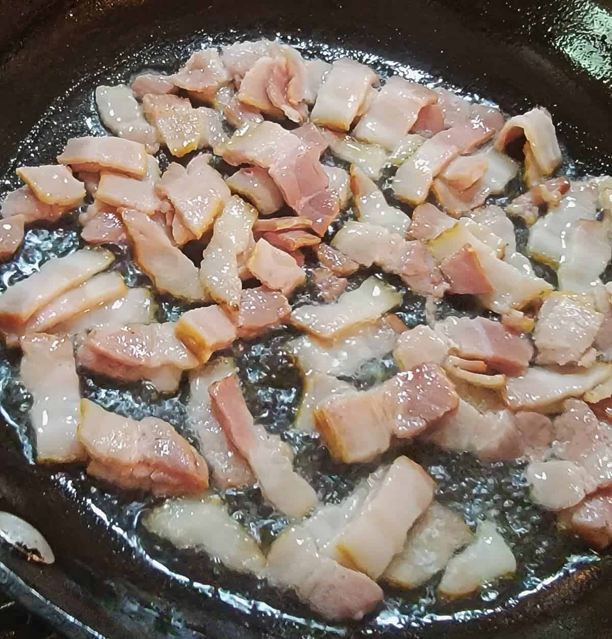 pieces of bacon beginning to fry in hot skillet