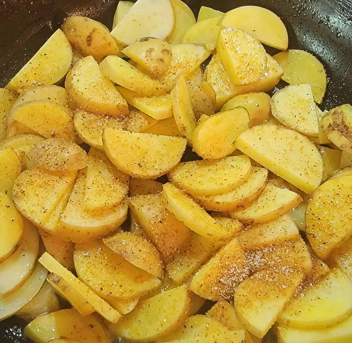 sliced yukon potatoes in skillet with seasoning sprinkled on top