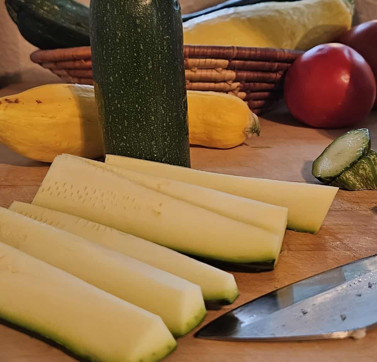 zucchini cut lengthwise into slices with a knife shown on a cutting board