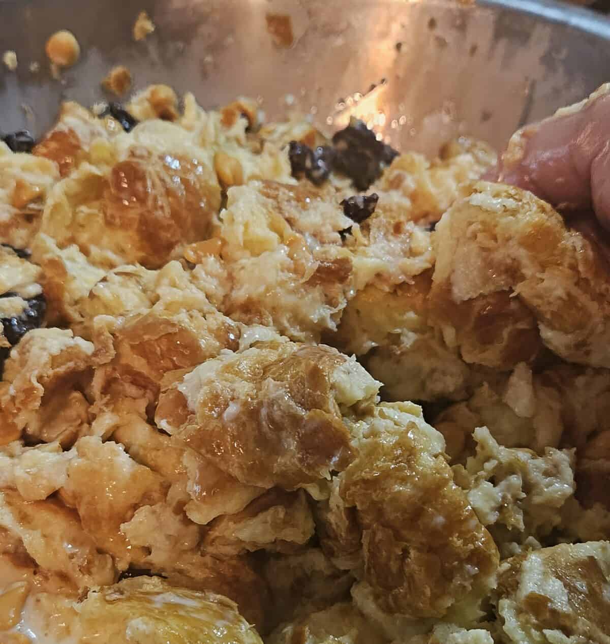 bread pudding mixture being mixed together by hand in a mixing bowl