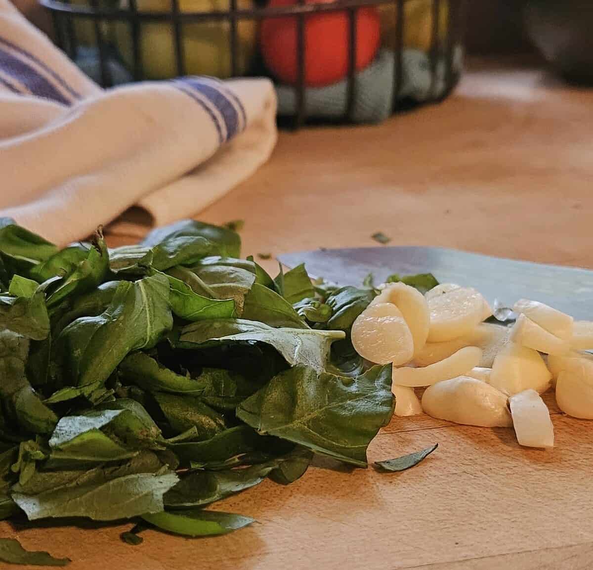 fresh garlic cloves and basil, cut into large pieces on wooden cutting board.