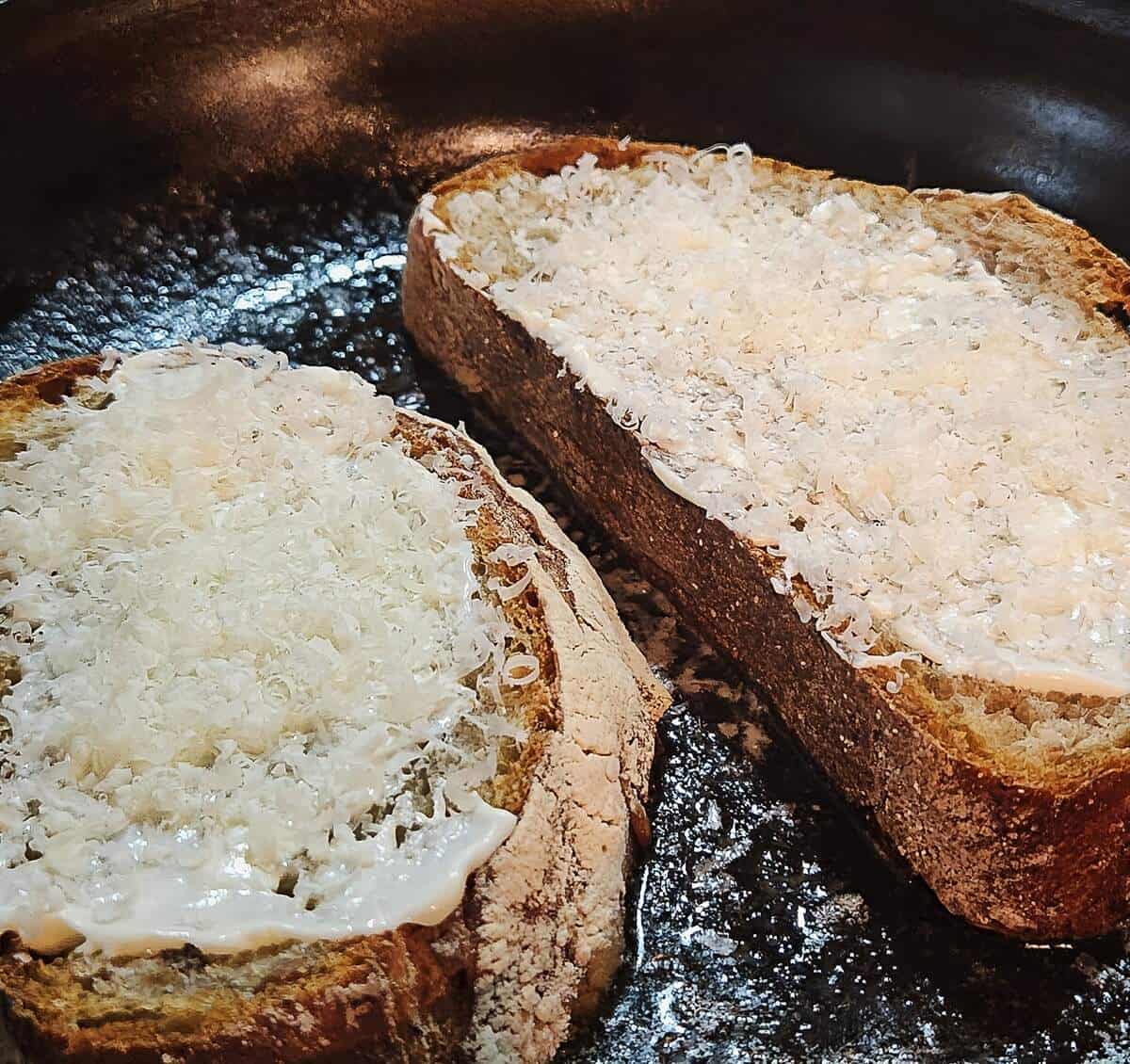 bread in pan, mayonnaise side up, with shredded parmesan cheese on top of mayo