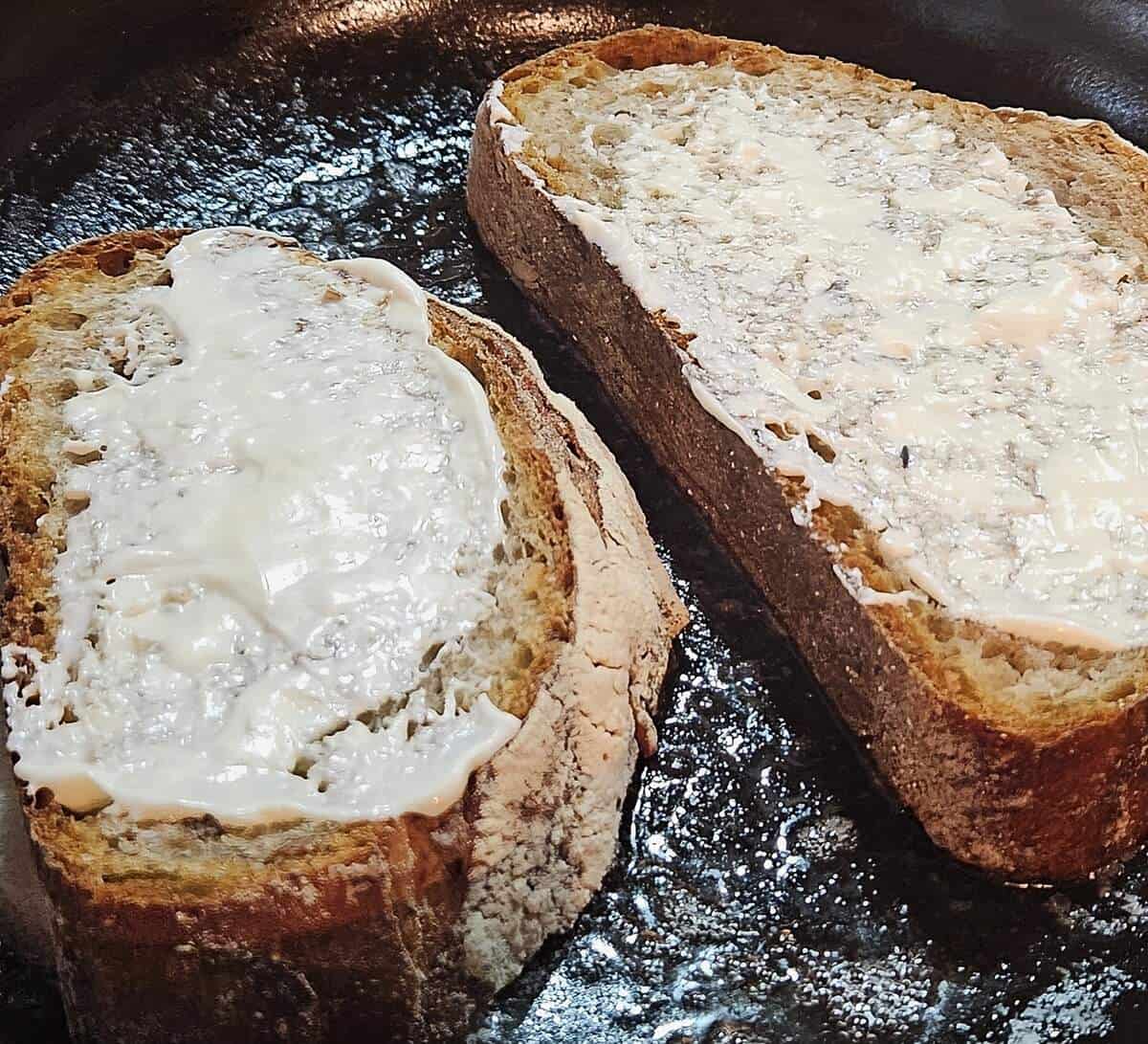 two slices of bread in pan with mayo shown spread on the side facing up