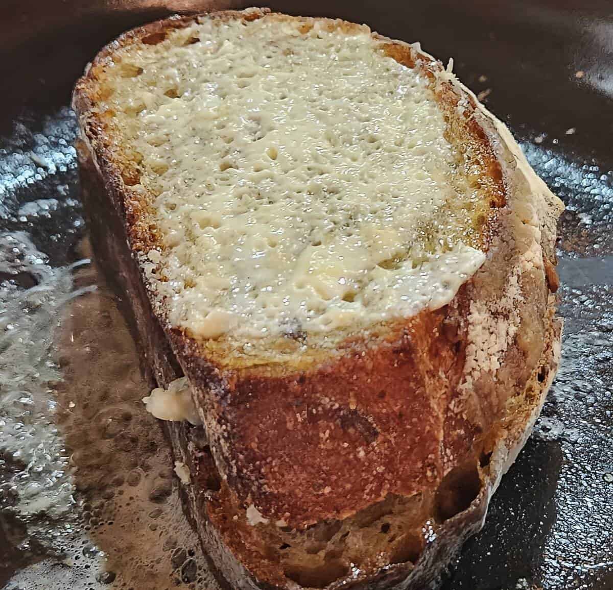 grilled cheese sandwich frying in pan, top bread showing slightly melted parmesan cheese crust