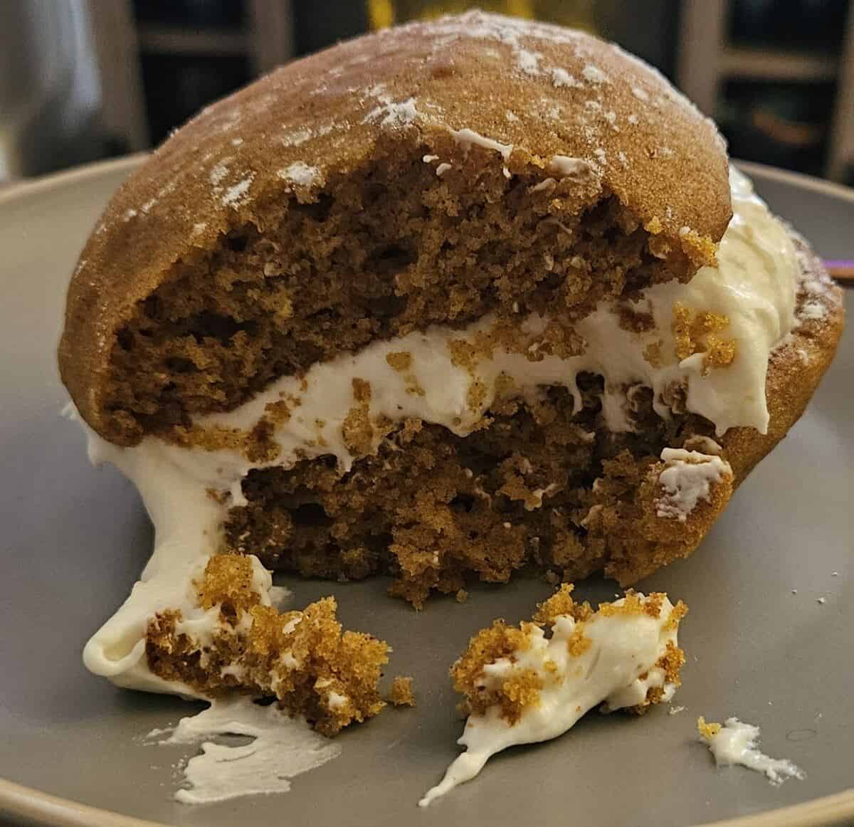 close up of finished whoopie pie cake sandwich, with a bite taken out, showing delicate cake crumbs and soft flowing cream cheese filling