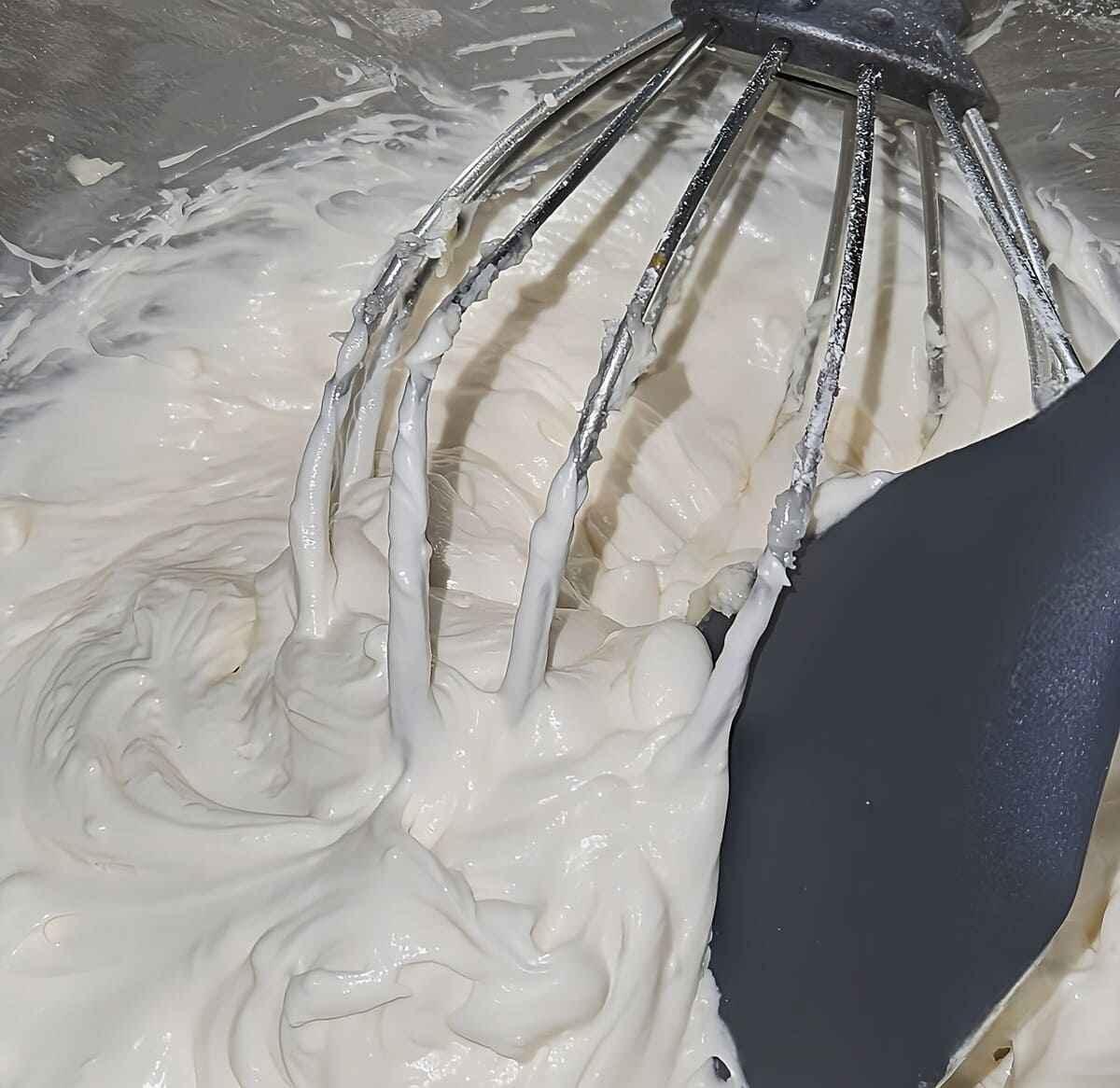 cream cheese filling for pumpkin whoopie pies, in mixer with ship attachment and rubber spatula in it, showing the appropriate color and shininess.