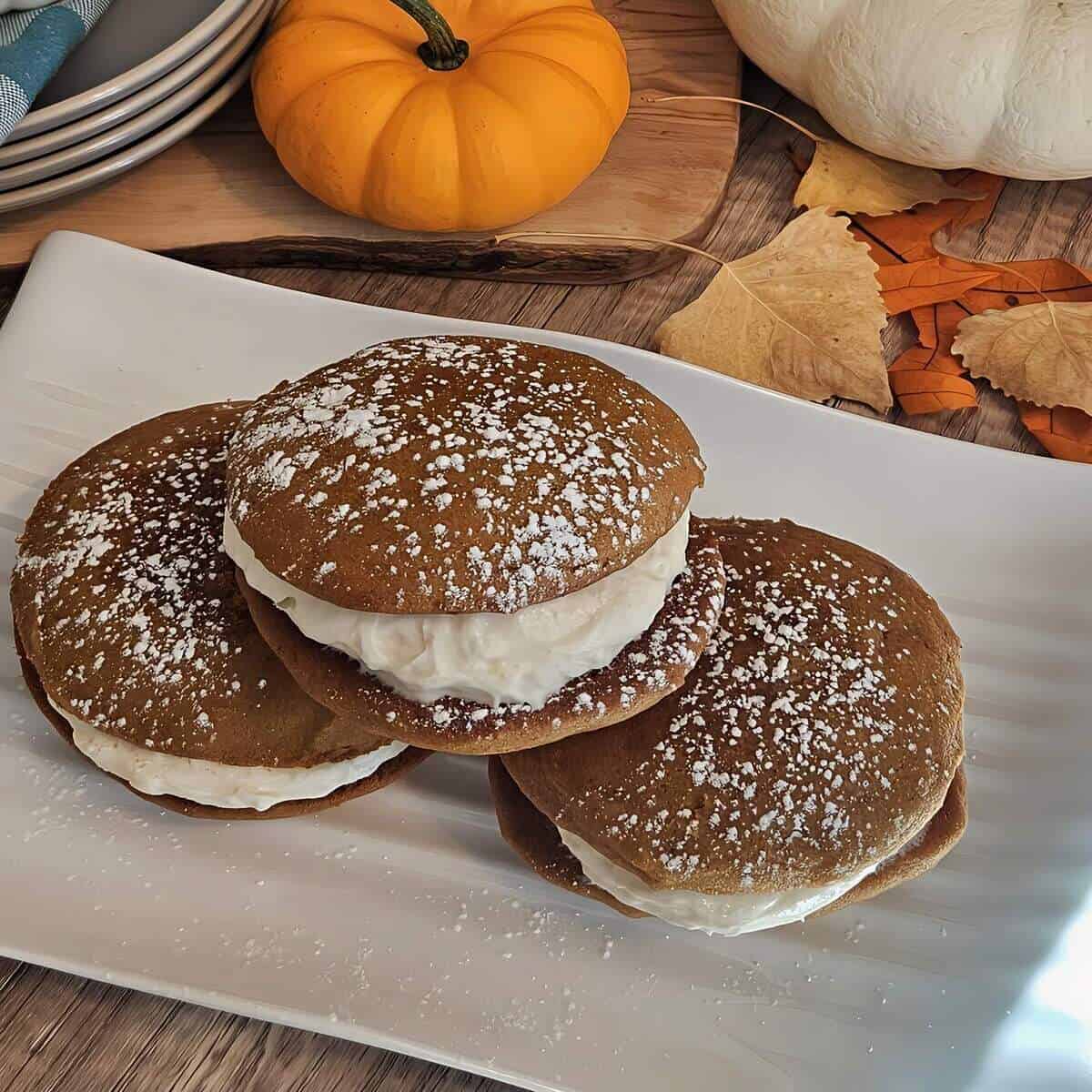 pumpkin spice whoopie pies with cream cheese filling and powdered sugar