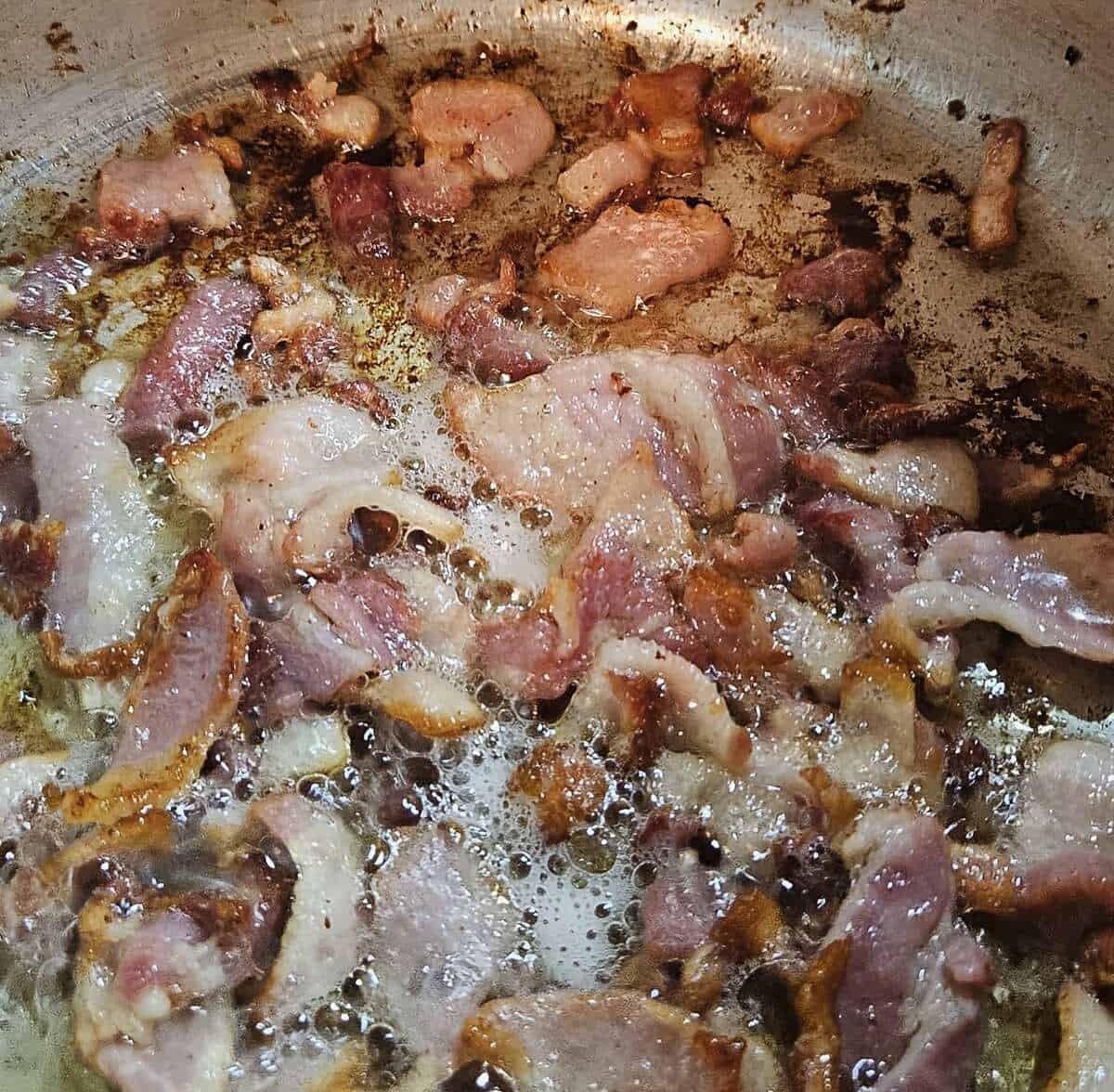 bacon pieces frying and releasing fat in saucepan.
