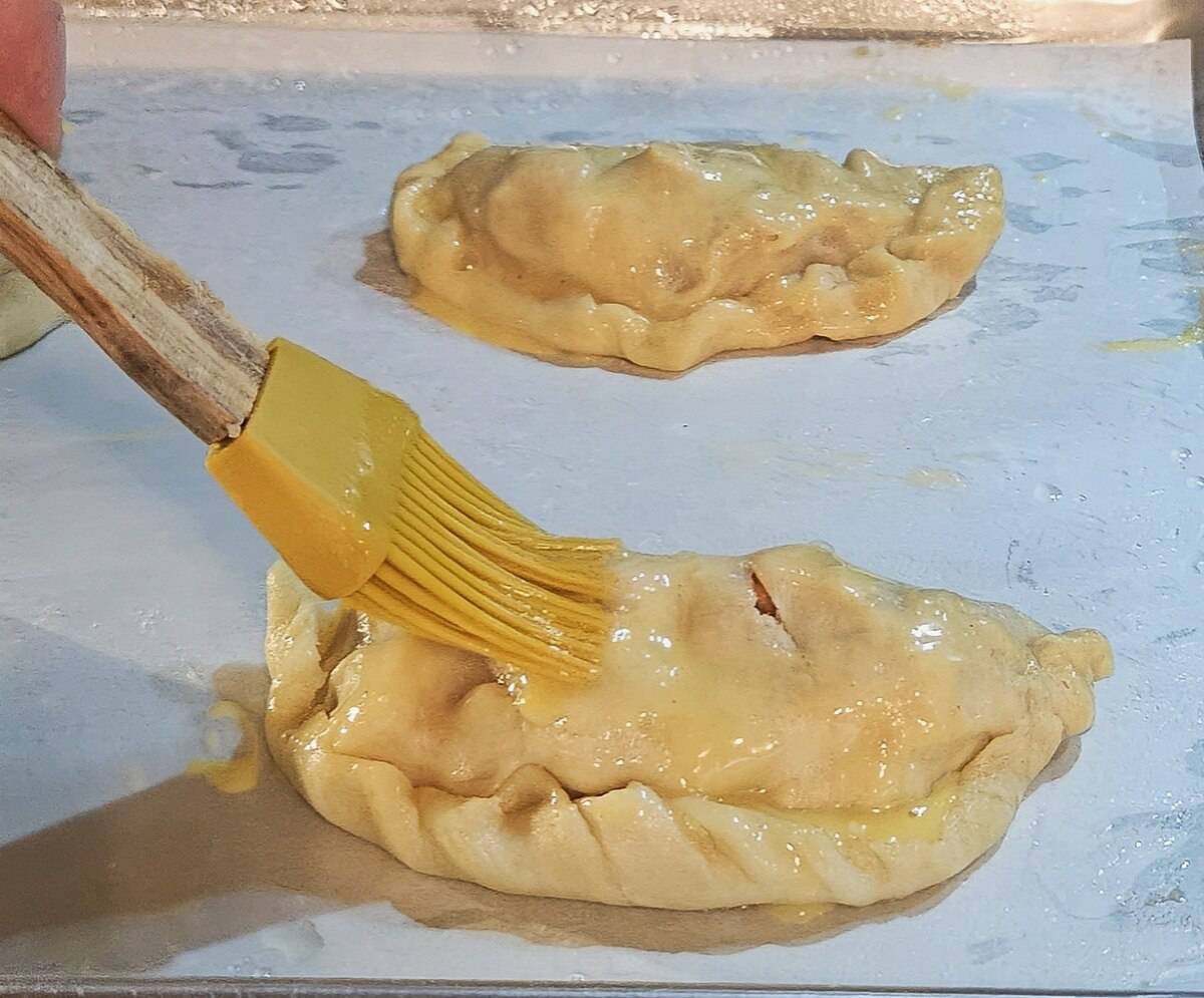 formed hand pies on a parchment lined sheet pan being brushed with egg wash