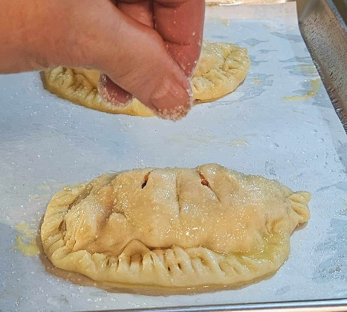 formed and egg washed empanadas being sprinkled with granulated sugar.