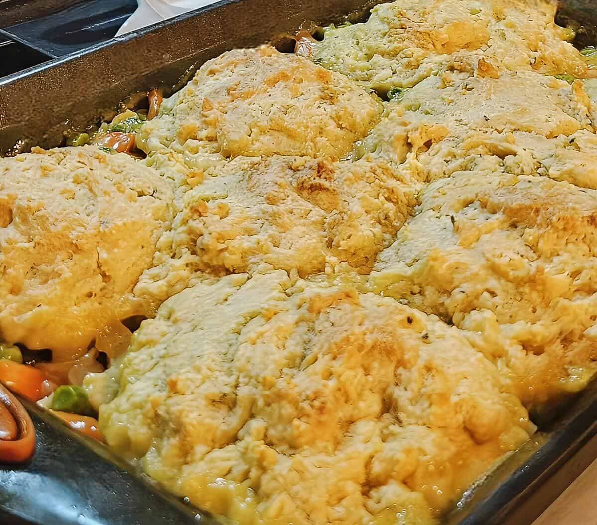 pan of chicken cobbler right after baking, biscuit topping browned on top, vegetables and sauce peeking from around edges of pan.