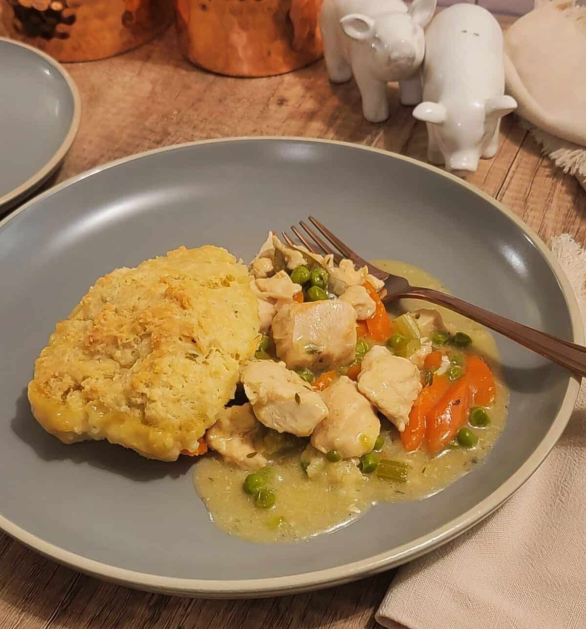 a plate of finished chicken cobbler with a fork, gravy and chunks of cooked chicken with vegetables, rosemary biscuit topping.