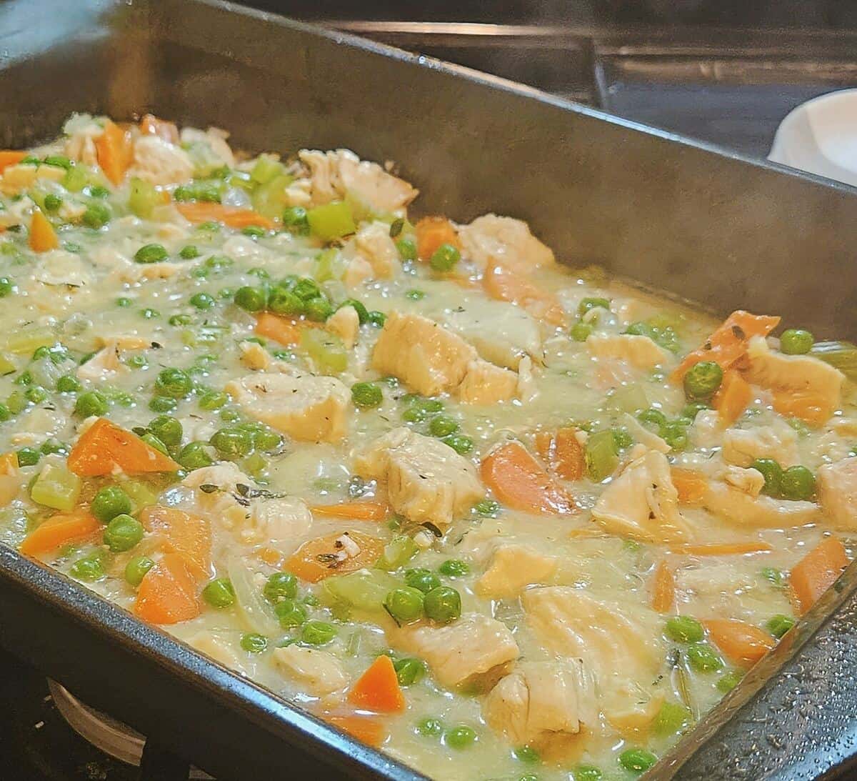 chicken cobbler gravy with chunks of chicken and vegetables in baking pan