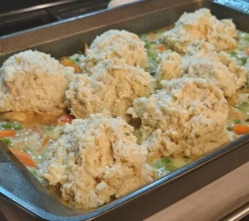 chicken cobbler in pan ready to bake, gravy with vegetables on bottom with biscuit dough scooped on top.