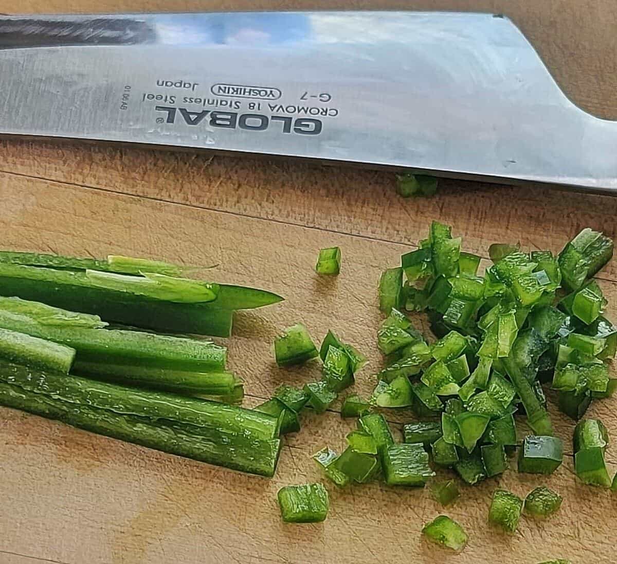 cored jalapeno, sliced into thin strips, and then again into very small dice, knife shown in background.