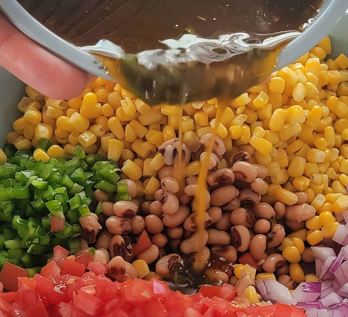 ingredients for cowboy caviar in a bowl with dressing being poured over.
