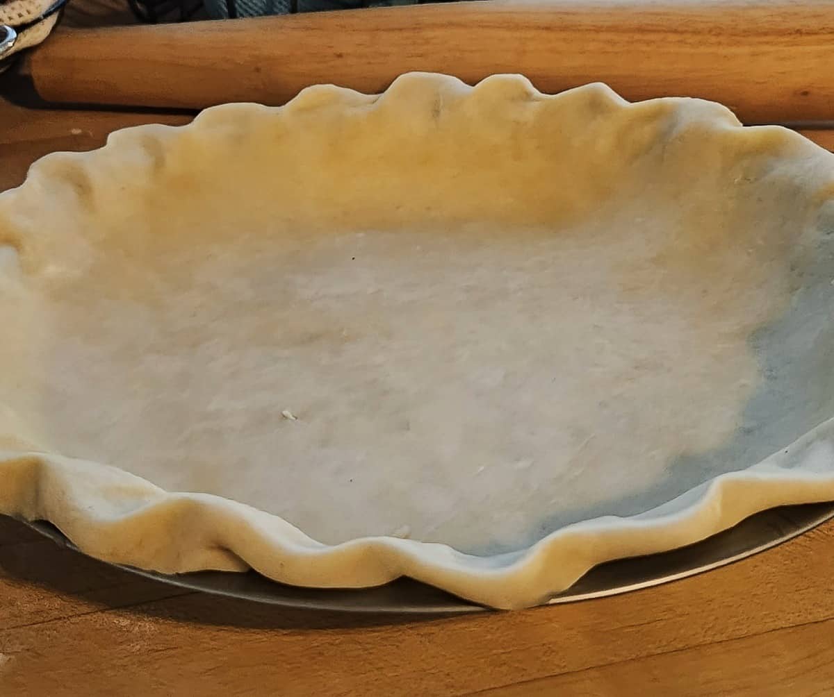 pie crust dough nested in pie pan with edges ruffled