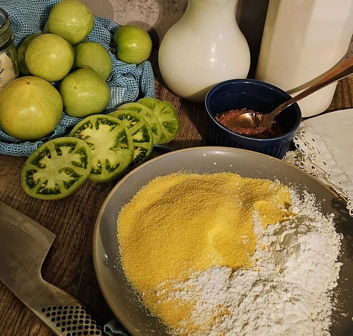ingredients for fried green tomatoes; green tomatoes, both in whole and sliced form, blackening spice blend, corn starch and corn meal, buttermilk