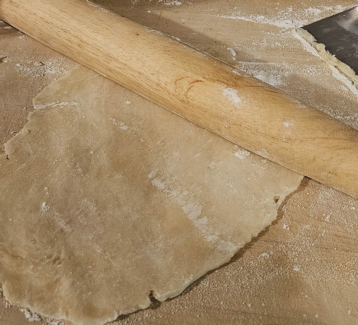 pie dough rolled out thinly with rolling pin on floured board
