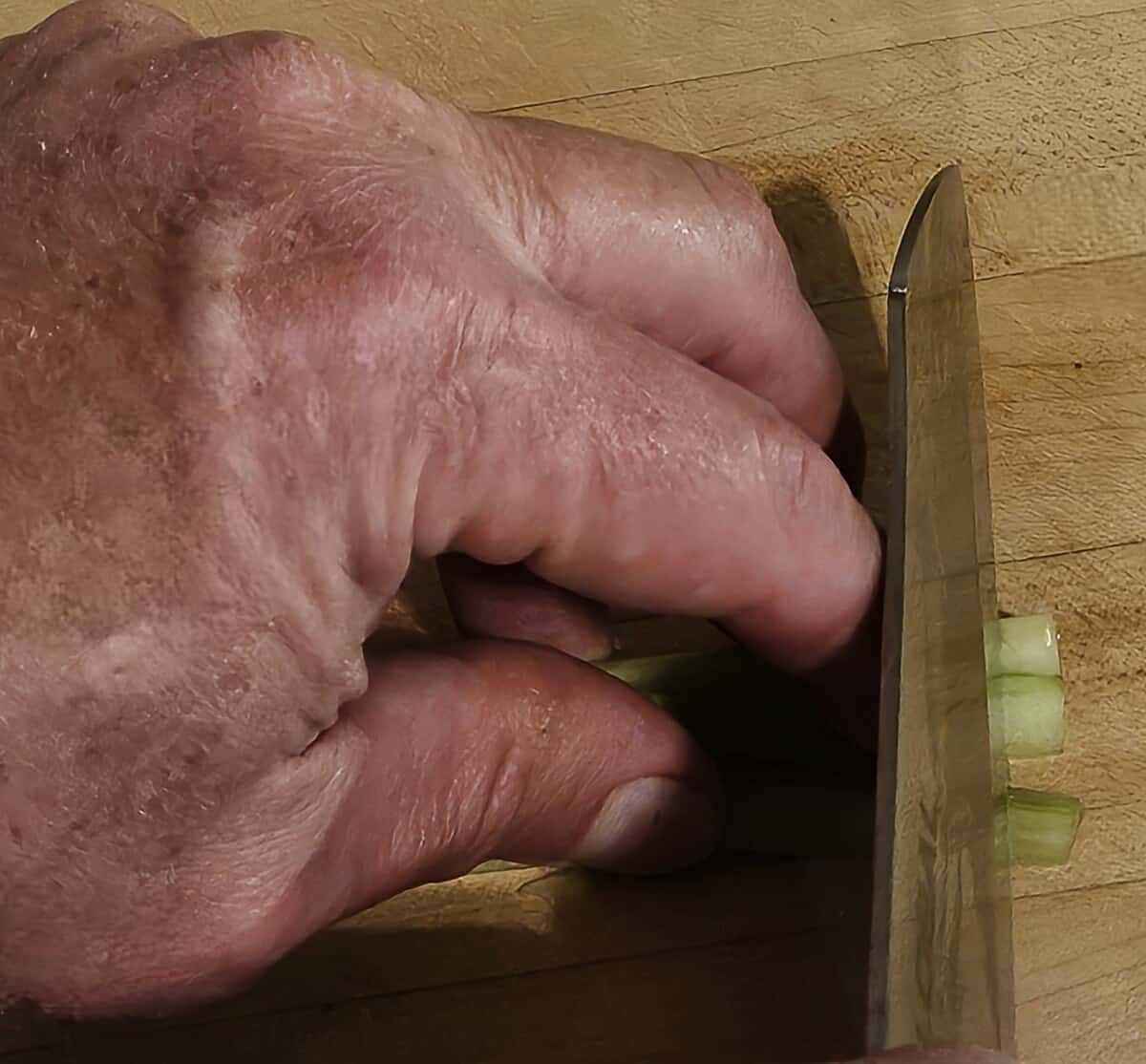 hand and knife cutting celery into brunoise dice, showing proper technique