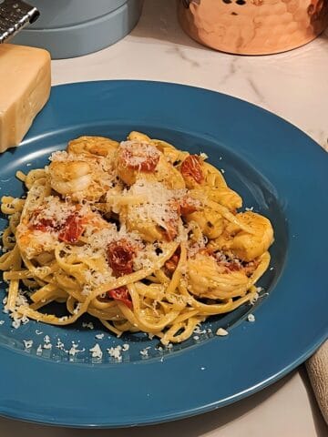 finished shrimp linguine pasta with pesto cream sauce, oven cured tomatoes on a plate covered with grated parmesan cheese.
