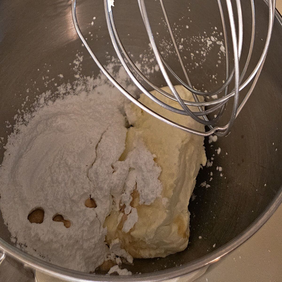 chunk of softened cream chees, powdered sugar, and vanilla extract in stand mixer bowl, with wire whip attachment.