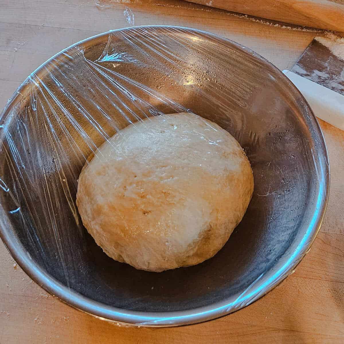 cinnamon roll dough in a mixing bowl wrapped over with plastic wrap.