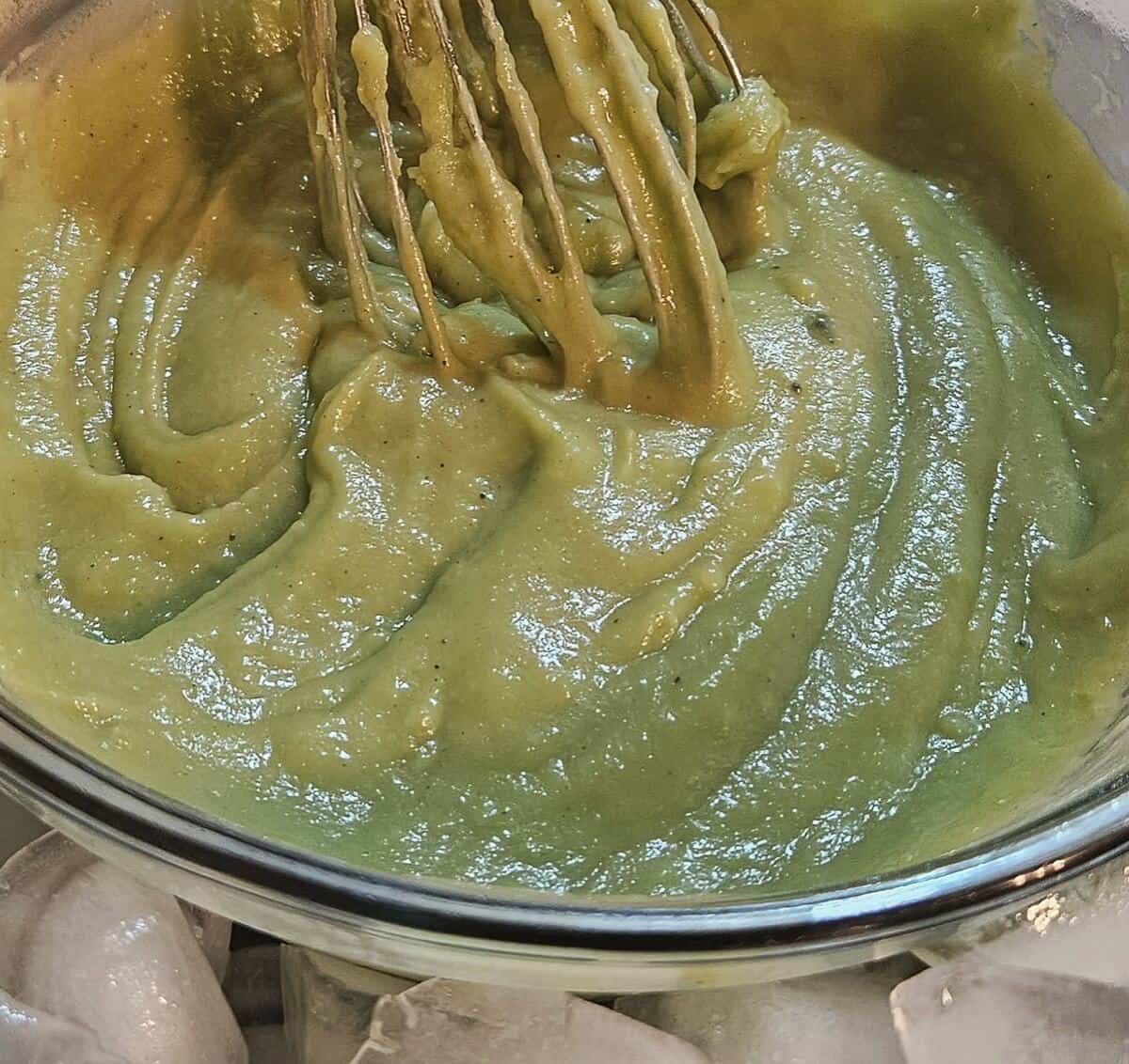 the finished matcha cream puff filling as it chills on an ice bath in a bowl while being stirred with a wire whip