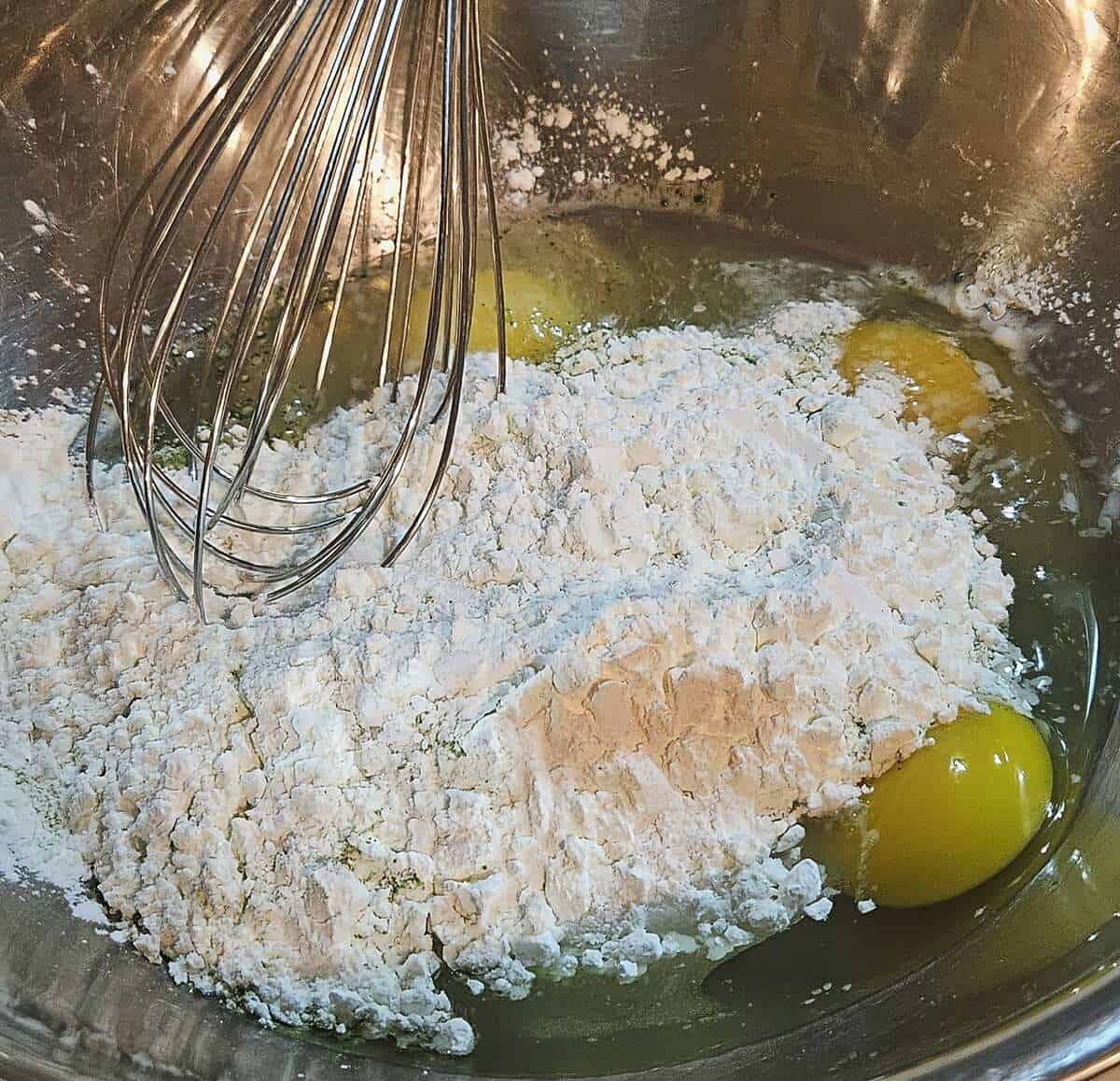 flour and eggs in a mixing bowl being stirred together with a wire whip.