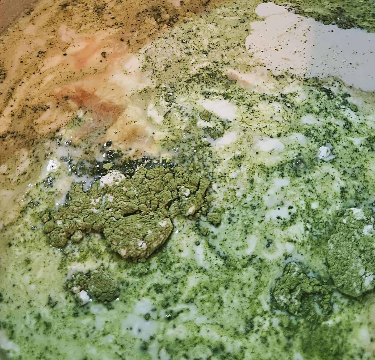 close up of ingredients to be heated in a saucepan. milk, vanilla extract, and green matcha powder floating on top.
