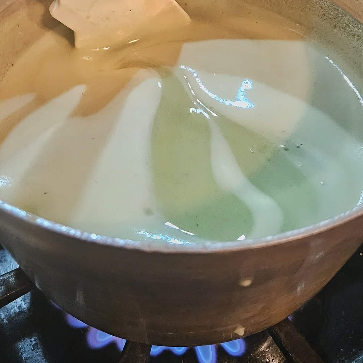 the matcha cream puff filling being gently heated while being stirred with a rubber spatula, showing a foam on top with the cream thickening as it heats.