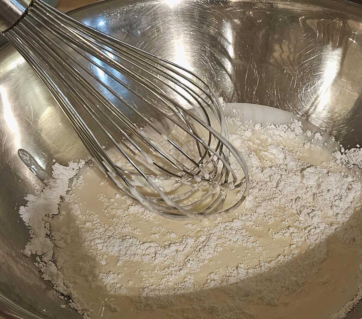 cream and powdered sugar in a bowl being whipped with a wire whip to eventually lighten the filling for matcha cream puffs