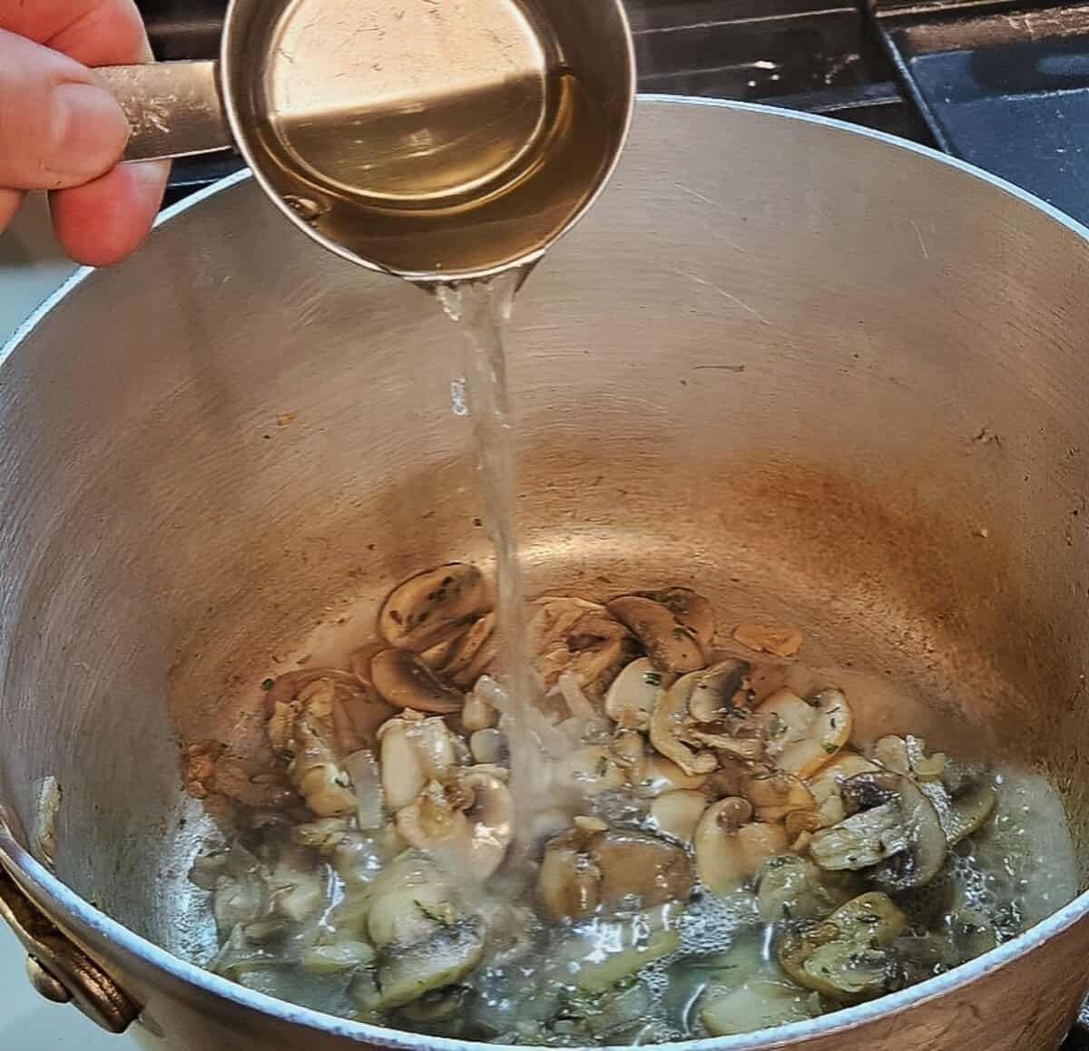 sautéed mushrooms, shallots,, garlic, and rosemary in a saucepan with white wine being poured in.