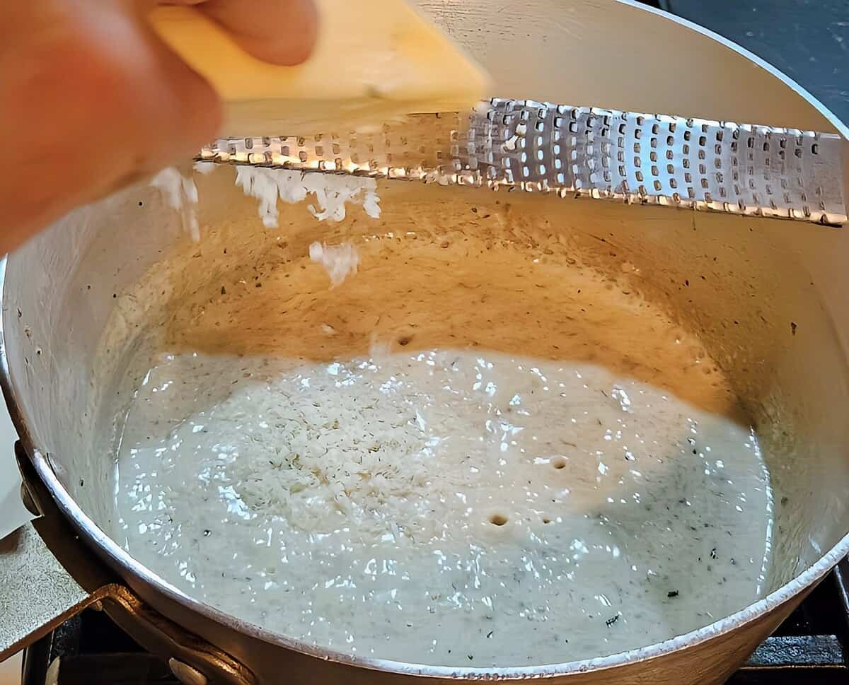 thickened mushroom soup simmering in a saucepan with asiago cheese being finely grated into the pot