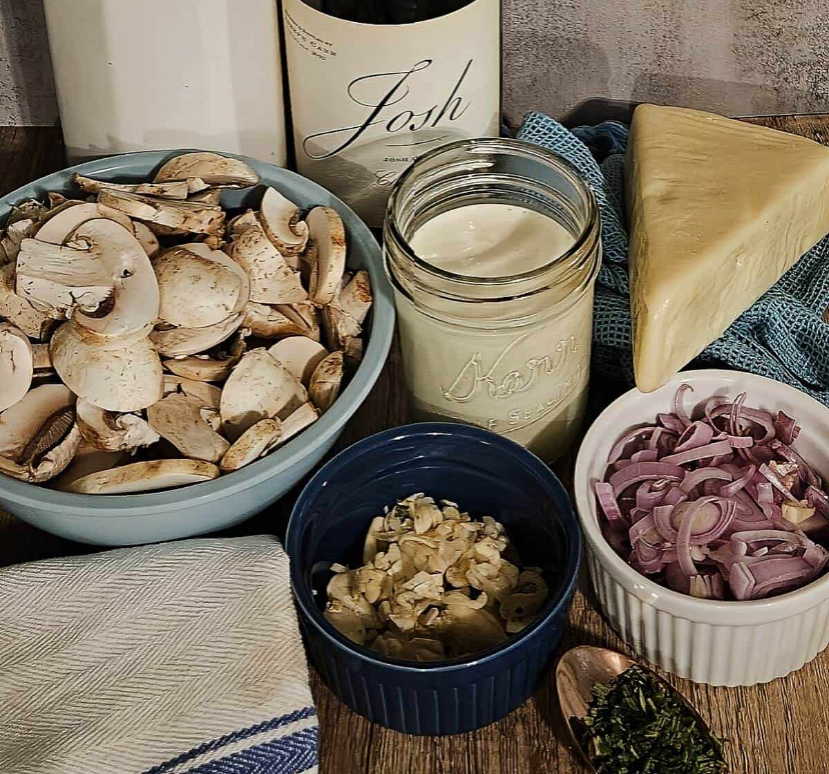 ingredients for creamy mushroom asiago soup; sliced mushrooms, cream and milk, asiago cheese, white wine, sliced shallots, chopped rosemary, and sliced garlic