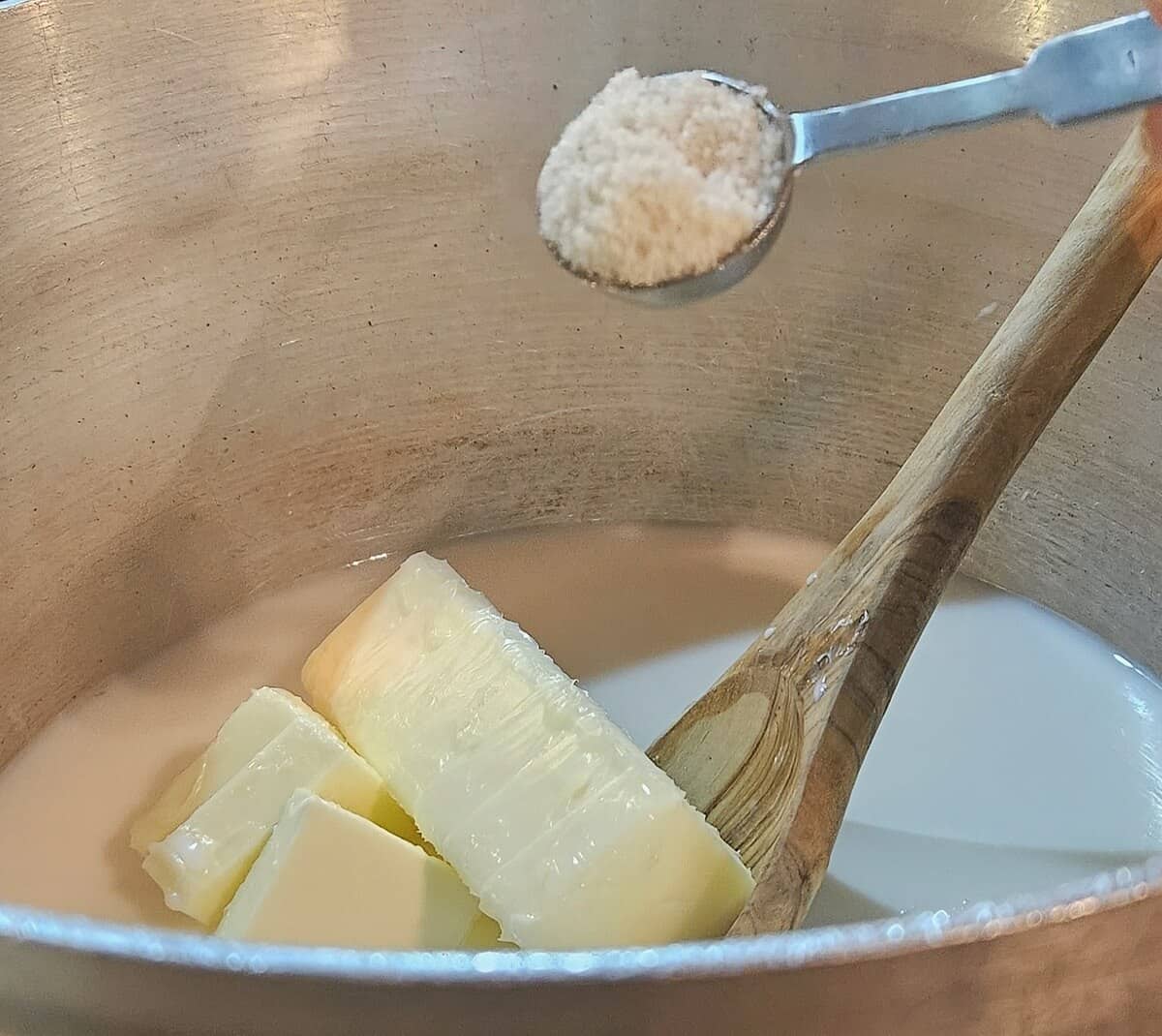 butter and water and milk mixture in a saucepan with a wooden spoon stirring it, a spoon of salt being added. process of making pate choux