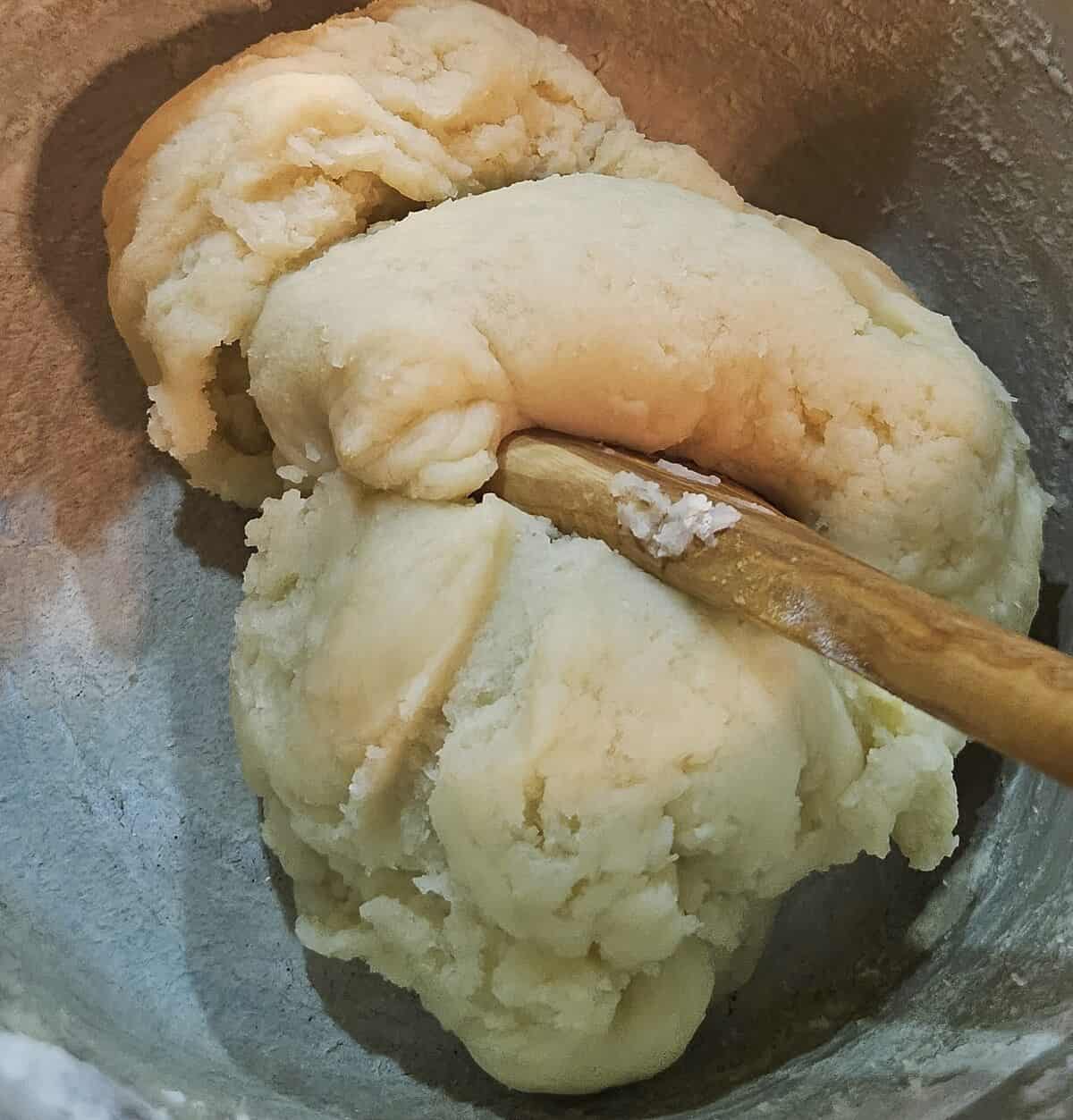 pate choux dough being stirred in a saucepan, showing the appropriate moisture level, as the ball of dough pulls away from the edges of the pan cleanly.