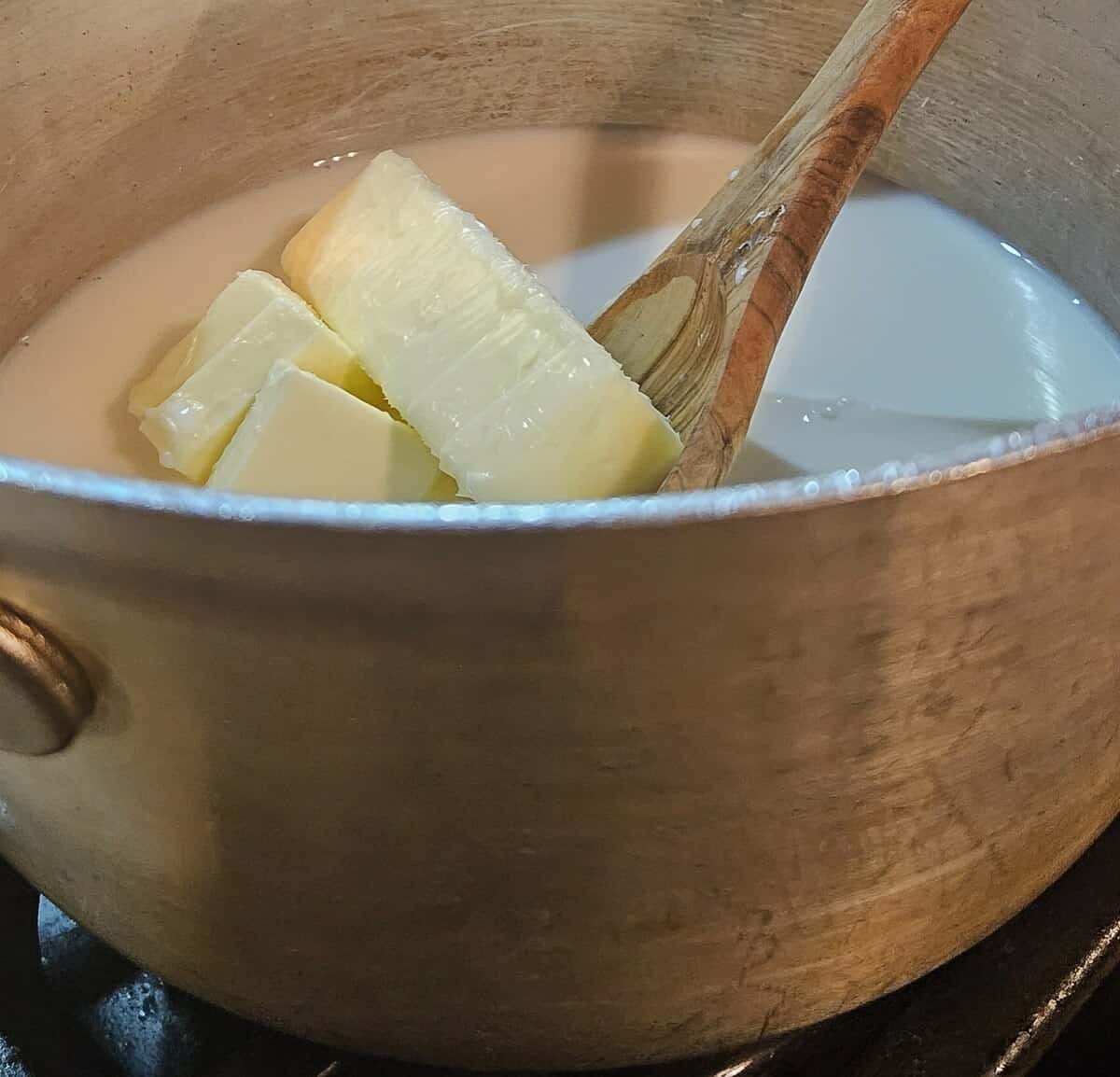 butter being stirred into milk and water in a saucepan on a stovetop